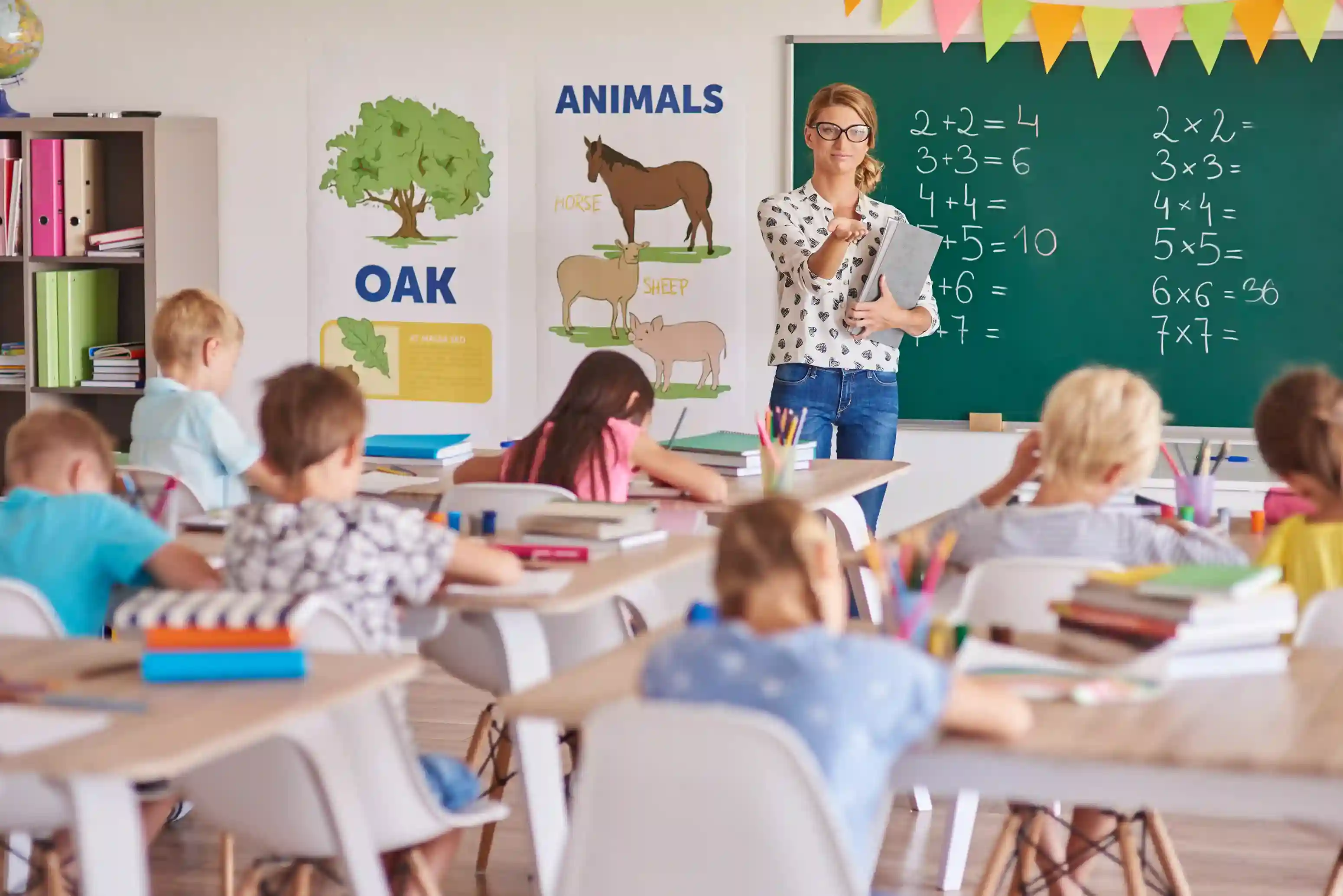Teacher guiding students in a classroom with a chalkboard, representing education and institutional learning environment.